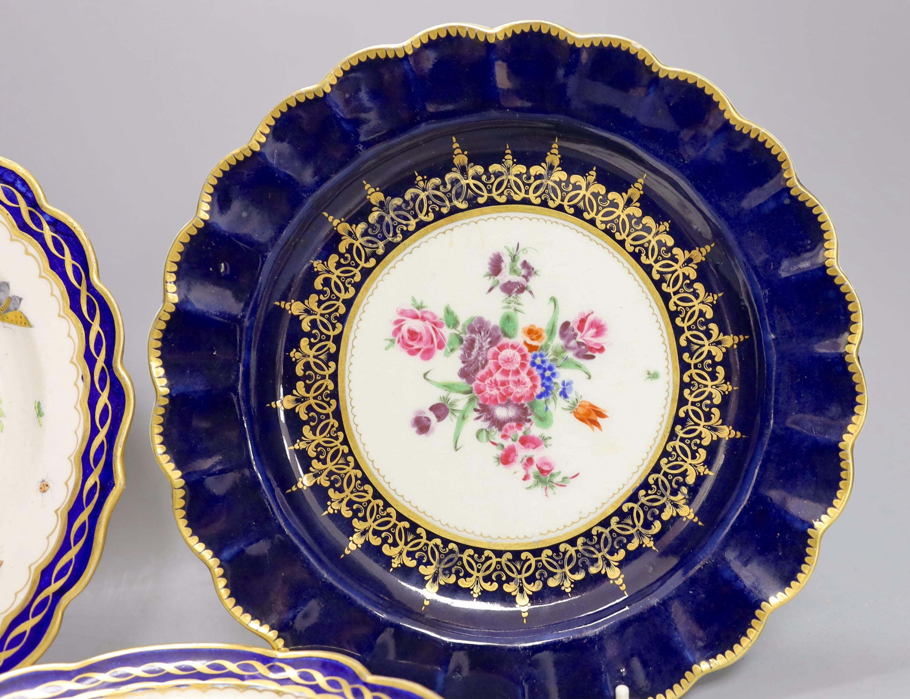 Three Worcester plates having blue border, one with elaborated gilding enclosing a bouquet of flowers, two plates both with a star shaped foliate design in the centre, c.1775, largest 21.5 cm